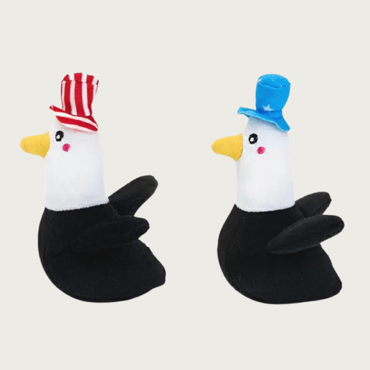 A pair of small, plush bald eagle dog toys. One is wearing a red & white striped top hat, the other is wearing a medium blue hat with white stars.