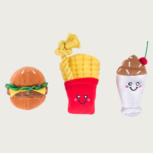 Three small, plush dog toys shaped like a cheeseburger, fries in red packaging, and chocolate milkshake with a cherry on top.