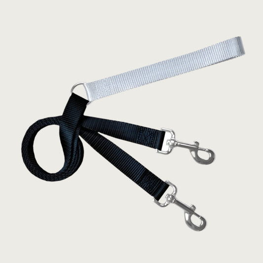 Dog leash with light gray loop handle with D-ring at its other end. The main part of the leash is black, and feeds through the D-ring on the handle. Each end of the black leash has a metal clip.