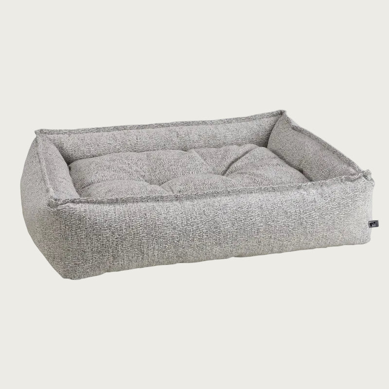 Low-profile, rectangular pet bed with bolsters and tufted center cushion. Color is a light gray with subtle black threads running throughout.
