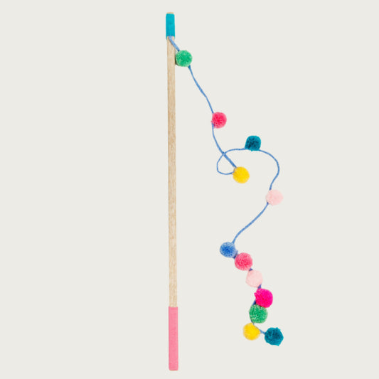 Wooden pole with yarn covered ends, with a long string attached at one end. The thick string has multiple pom pom balls attached in assorted colors, and unevenly spaced.