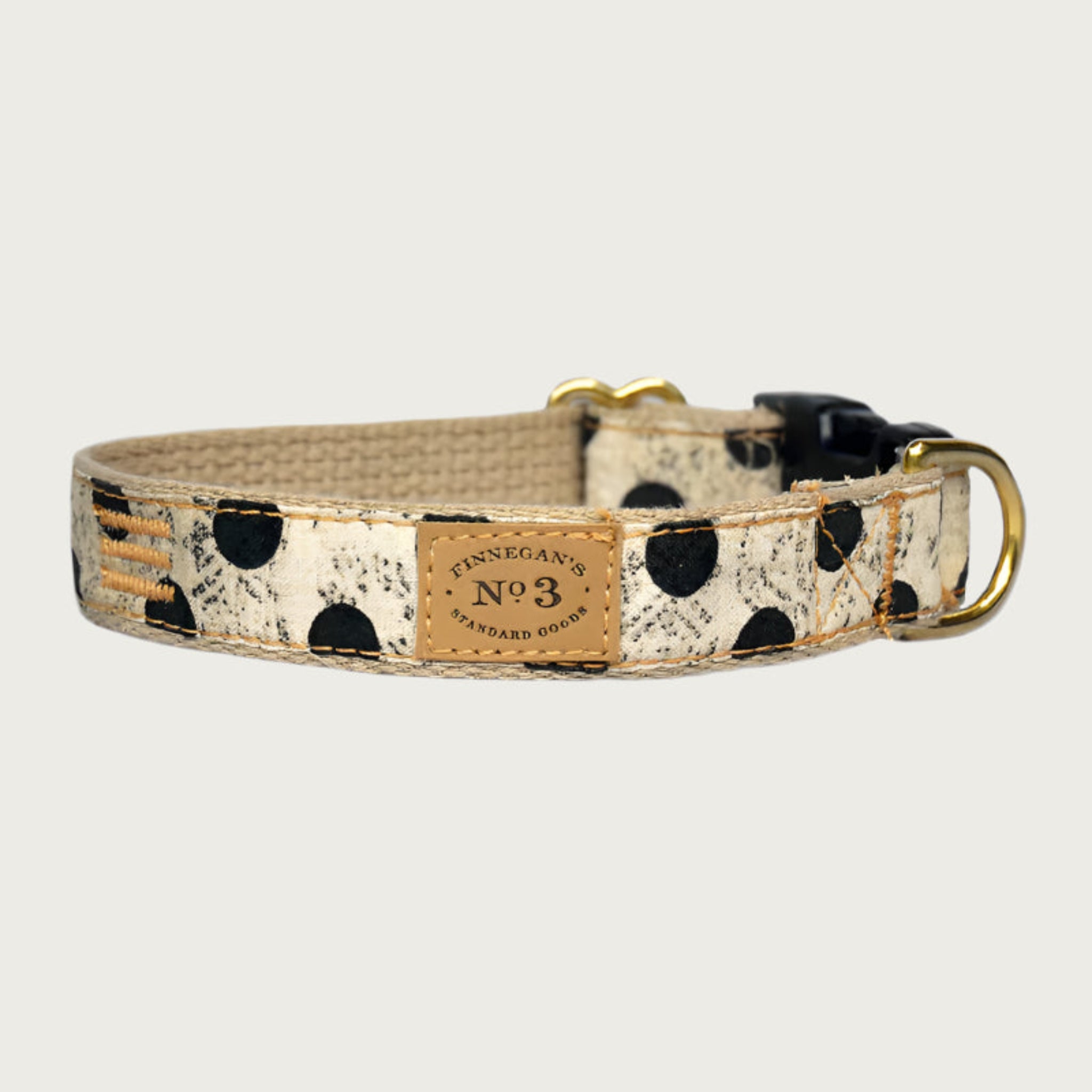 Creamy beige dog collar with large black polka dots, with a subtle, muted black swirl pattern behind the dots. Black plastic buckle and brass D-ring.