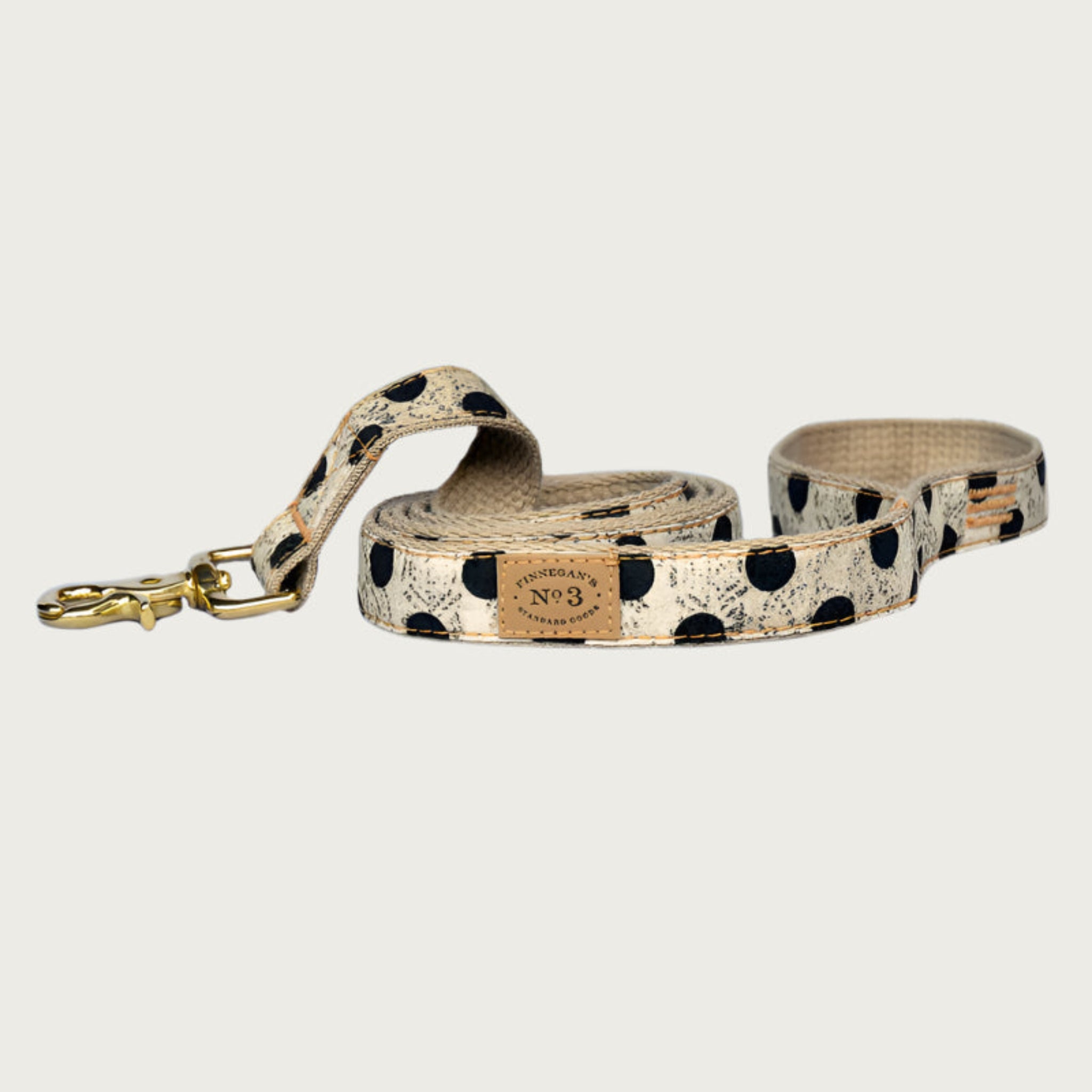 Creamy beige dog leash with large black polka dots, with a subtle, muted black swirl pattern behind the dots. Brass clasp.