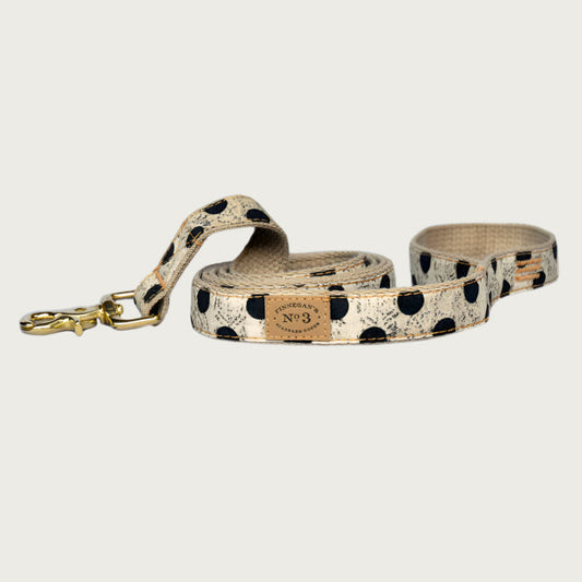 Creamy beige dog leash with large black polka dots, with a subtle, muted black swirl pattern behind the dots. Brass clasp.