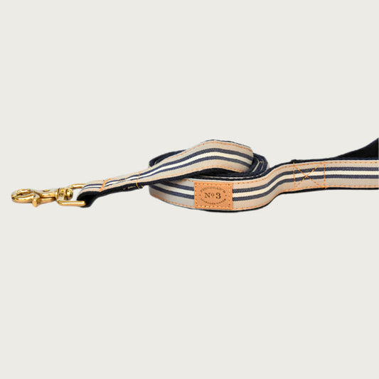 Dog leash with simple vertical striped pattern. Base colors is beige, with narrow navy blue and white stripes.
