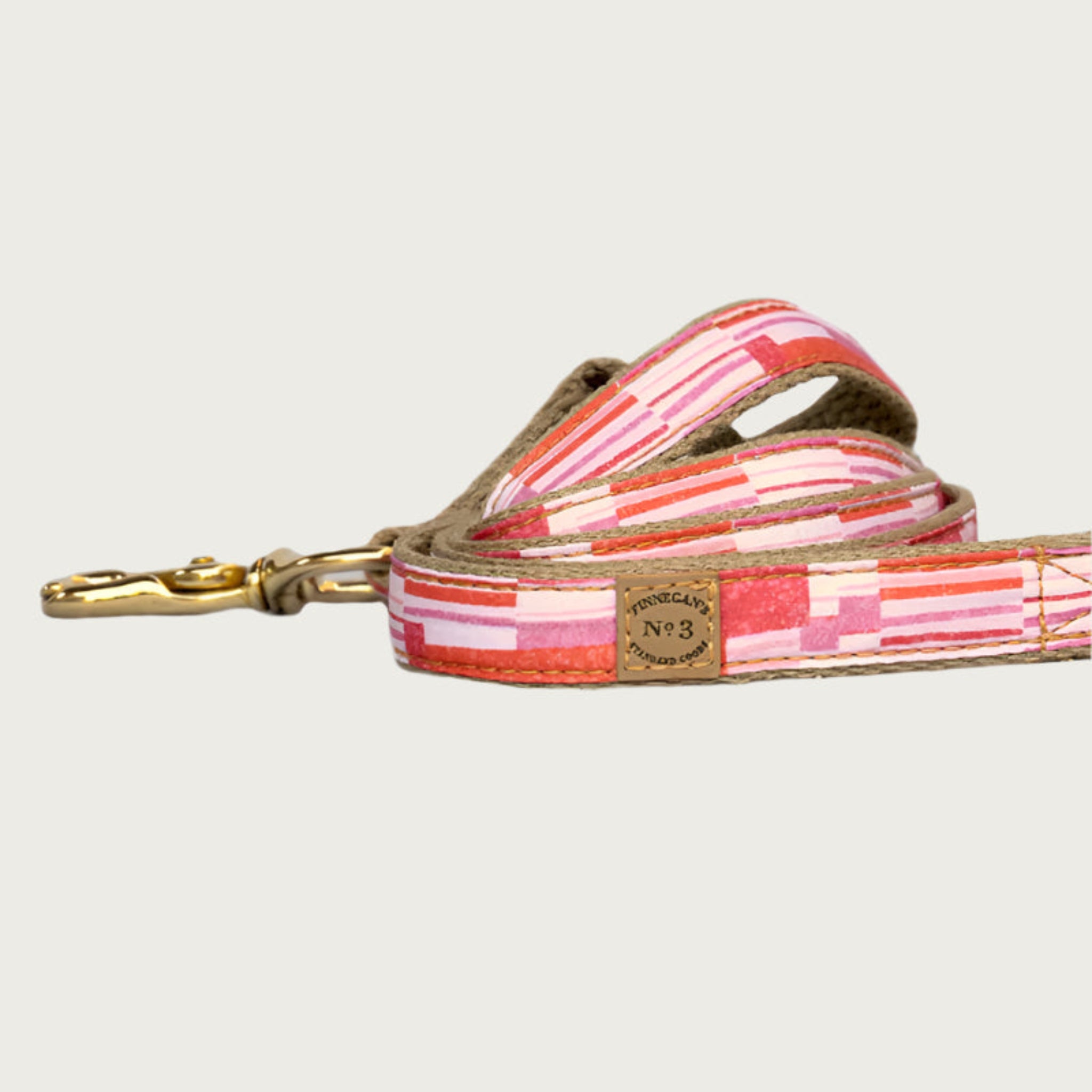 Dog leash with vertical, geometrical striped pattern in shades of orange, pink, and white.