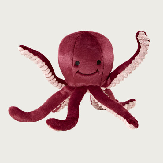 Plush Olympia Octopus dog toy from Fluff & Tuff. Its body is cranberry colored, with the underside of its legs a light pink with ribbed texture. It has a cute smiley face (eyes & mouth) embroidered in black on its head.