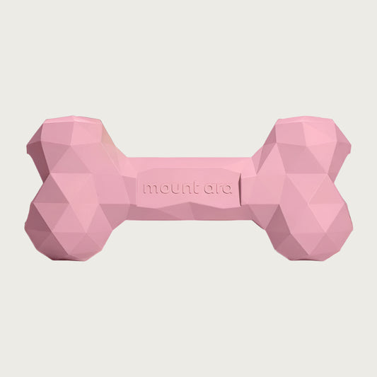 A pink, heavy rubber dog bone toy with geometric texture.