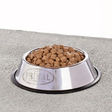 A stainless steel pet food bowl, filled with bite-sized morsels of Primal Pronto dog food.