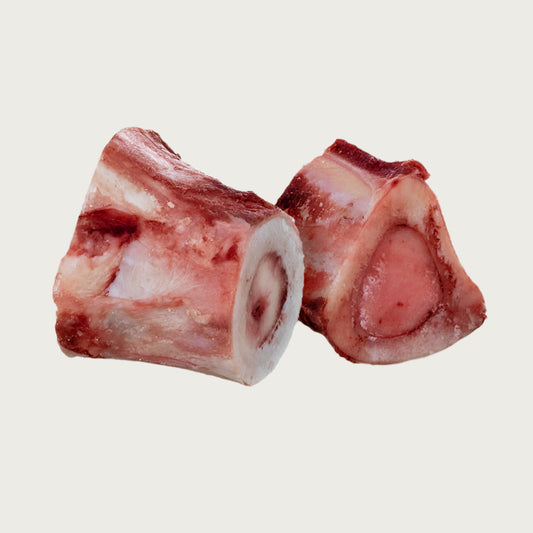 Two Primal beef marrow bones side by side, each is 2" to 3" long, showing close up detail of meaty exterior and marrow in the center. 