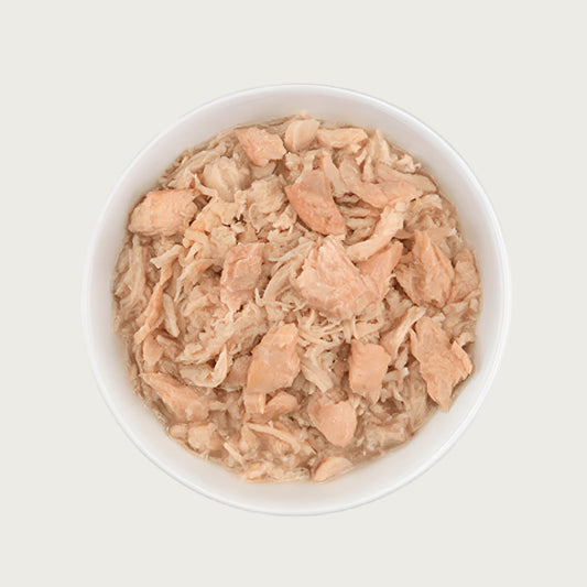 Close-up photo of a dish of Tiki Cat Wild Salmon & Chicken Recipe. Dish is full of shredded chicken and topped with large flakes of salmon.