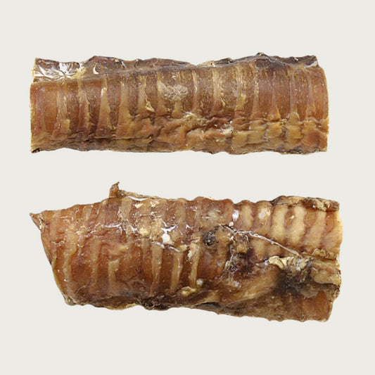 Two 6" long windee dog chews, side by side to show size & color variation. They are thin, hollow (with openings about 2" wide) and shaped like a stubby cylindrical stick.They are brownish tan colored and have a slightly bumpy texture.