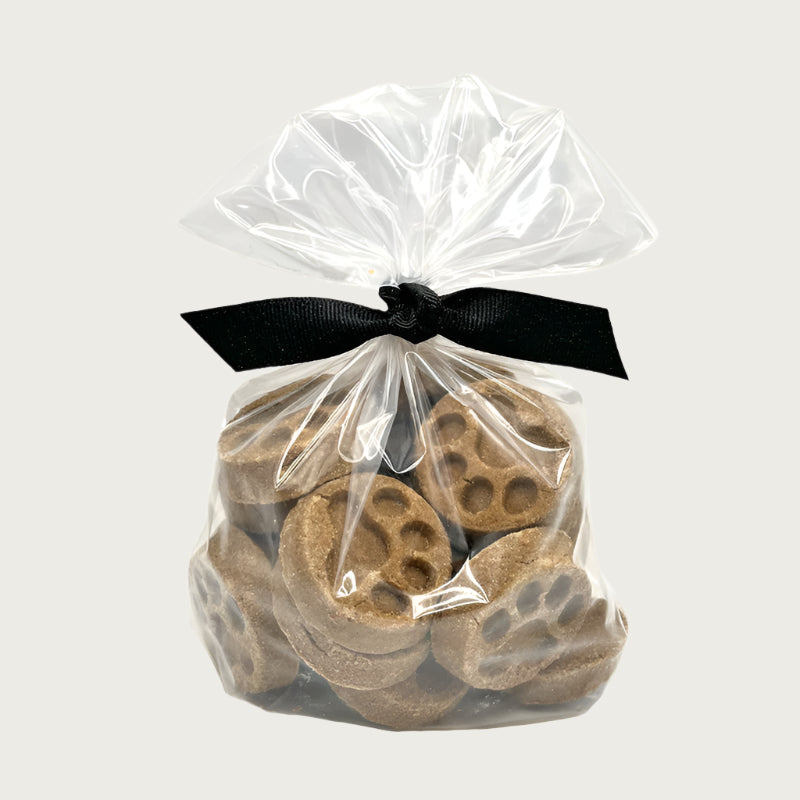 10 oz clear, resealable bag of Wet Nose exclusive, Apple Honey Paw Print dog treats, tied with black ribbon. Visible inside are 1.5"- 2" sized brown round cookies with embossed paw print.