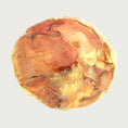 Load image into Gallery viewer, A round, flat dog chew in varying shades of tan and reddish brown.
