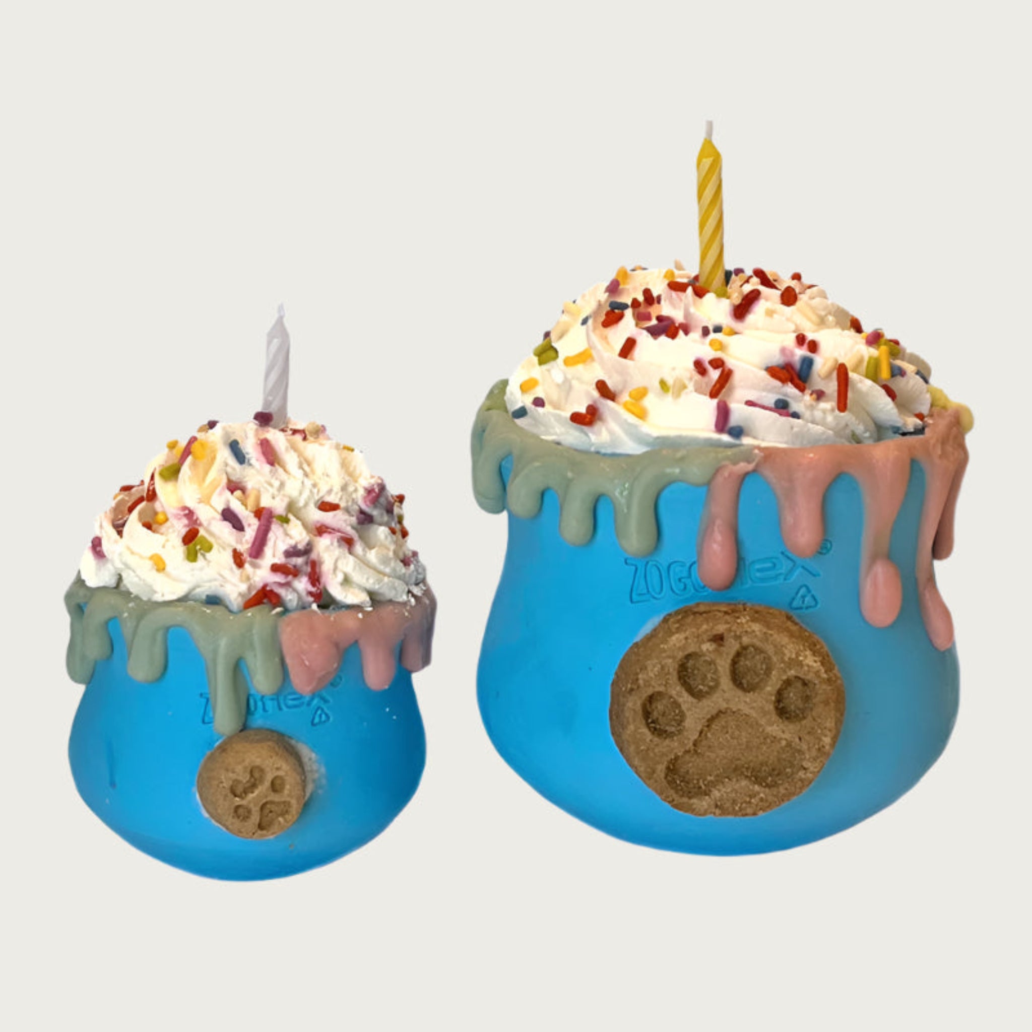 Small and large Celebration Toppls side by side to show size difference. They are cup shaped, blue dog toys, with whipped cream layered on top. There are multicolored sprinkles and a candle on top of the whipped cream. Dripping about halfway down the sides of the toy, is an edible, decorative drip design moving down from the rim of the toy.