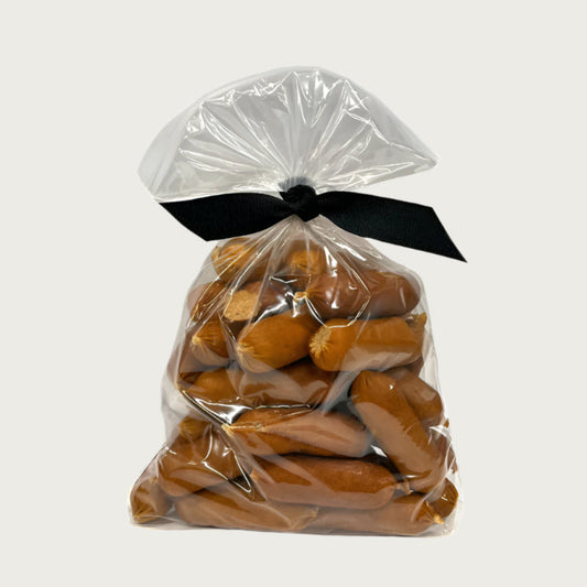 7 oz clear resealable bag of Wet Nose exclusive, Chicken Smokies dog treats, tied with black ribbon. Product inside is light brown colored links. 