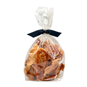 8 oz clear cellophane bag of Wet Nose exclusive Chicken Strips dog treats, tied with black ribbon. Inside are strips of chicken tenders, that are pale orangey-tan in color.