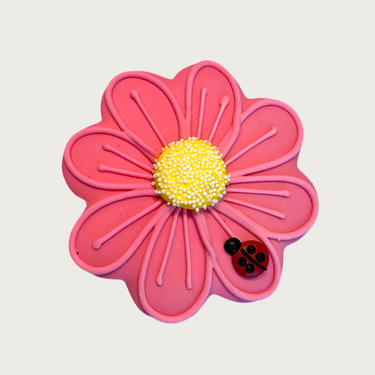 Pink daisy-shaped dog cookie with a yellow center and ladybug on the bottom right corner.