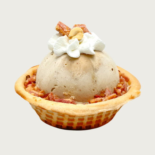Doggie Ice cream dessert with a scoop of tan colored ice cream in a waffle bowl, topped with a dollop of whipped cream, peanut halves and small pieces of bacon.