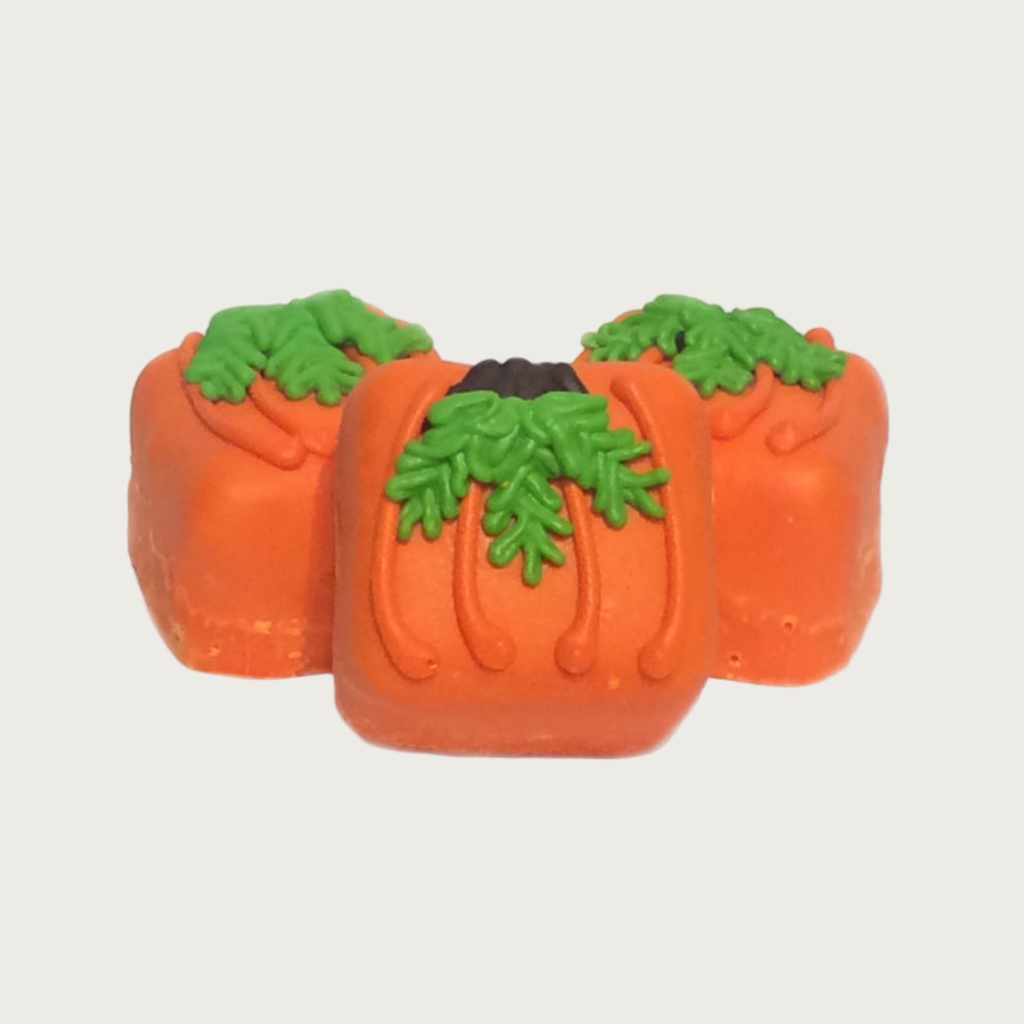 Three square Bon Bon dog treats, decorated to look like pumpkins. Body is orange, and iced with a brown "stem" and green "vines" trailing down.