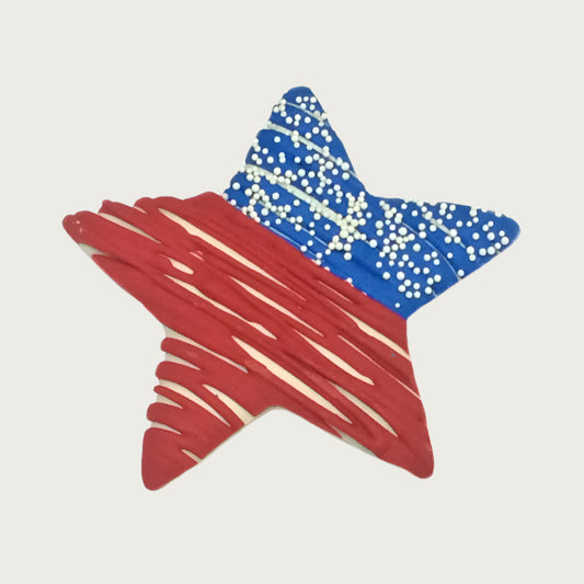 Star-shaped dog cookie decorated like the US flag with red and blue drizzle, with white nonpareil sprinkles.