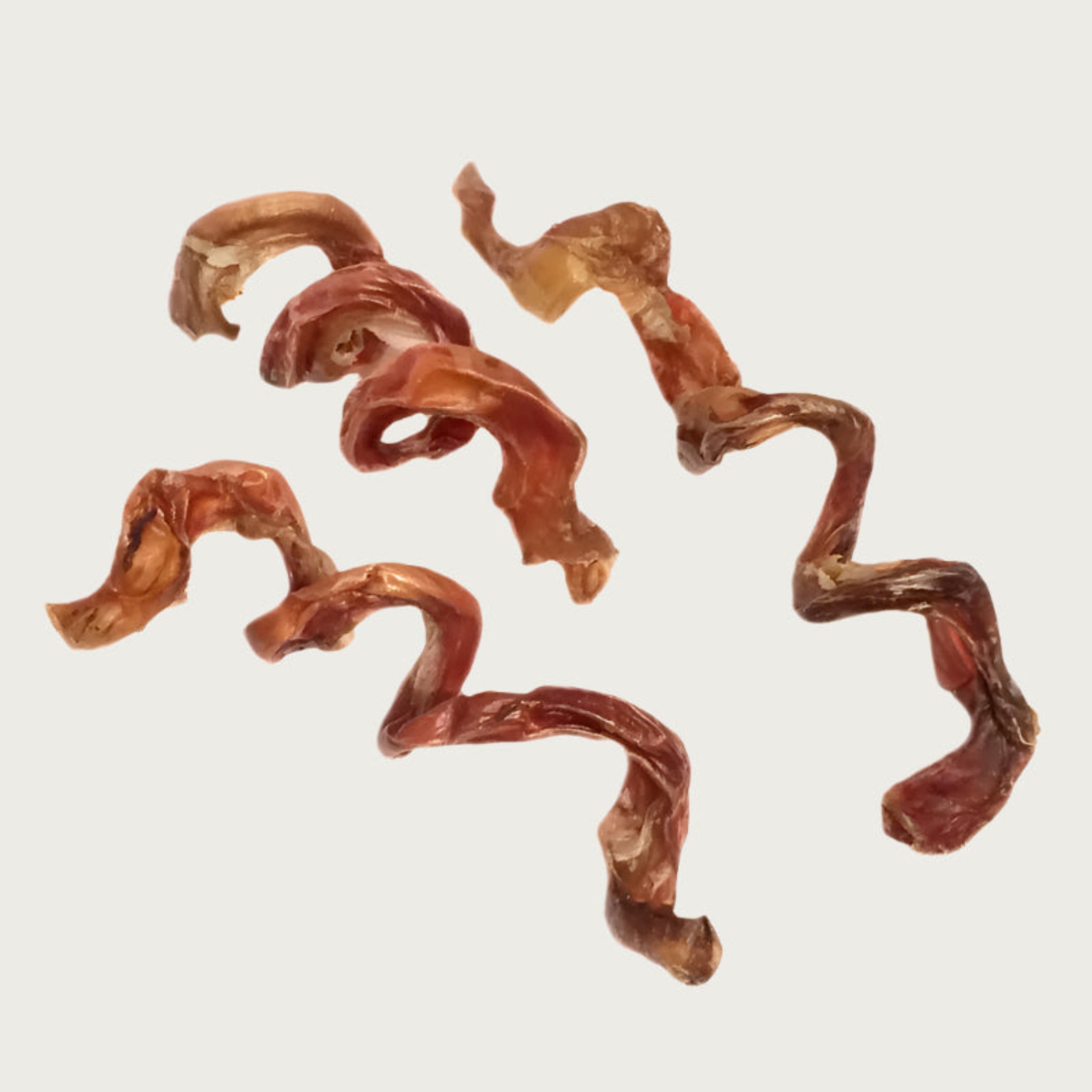 Three Flossie dog chews, side by side to show variations in size and shape. They are reddish brown in color, and have a spring-like shape.