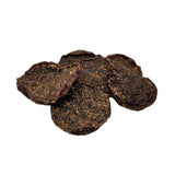 A close-up photo of a small pile of Wet Nose Sliders dog treats. They are round discs, about 2" wide, and dark brown in color.